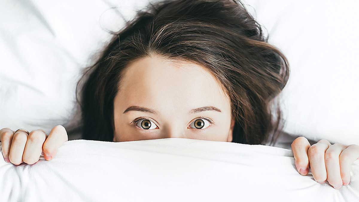 Junge Frau versteckt sich unter einer Bettdecke - Photo by Alexandra Gorn on Unsplash